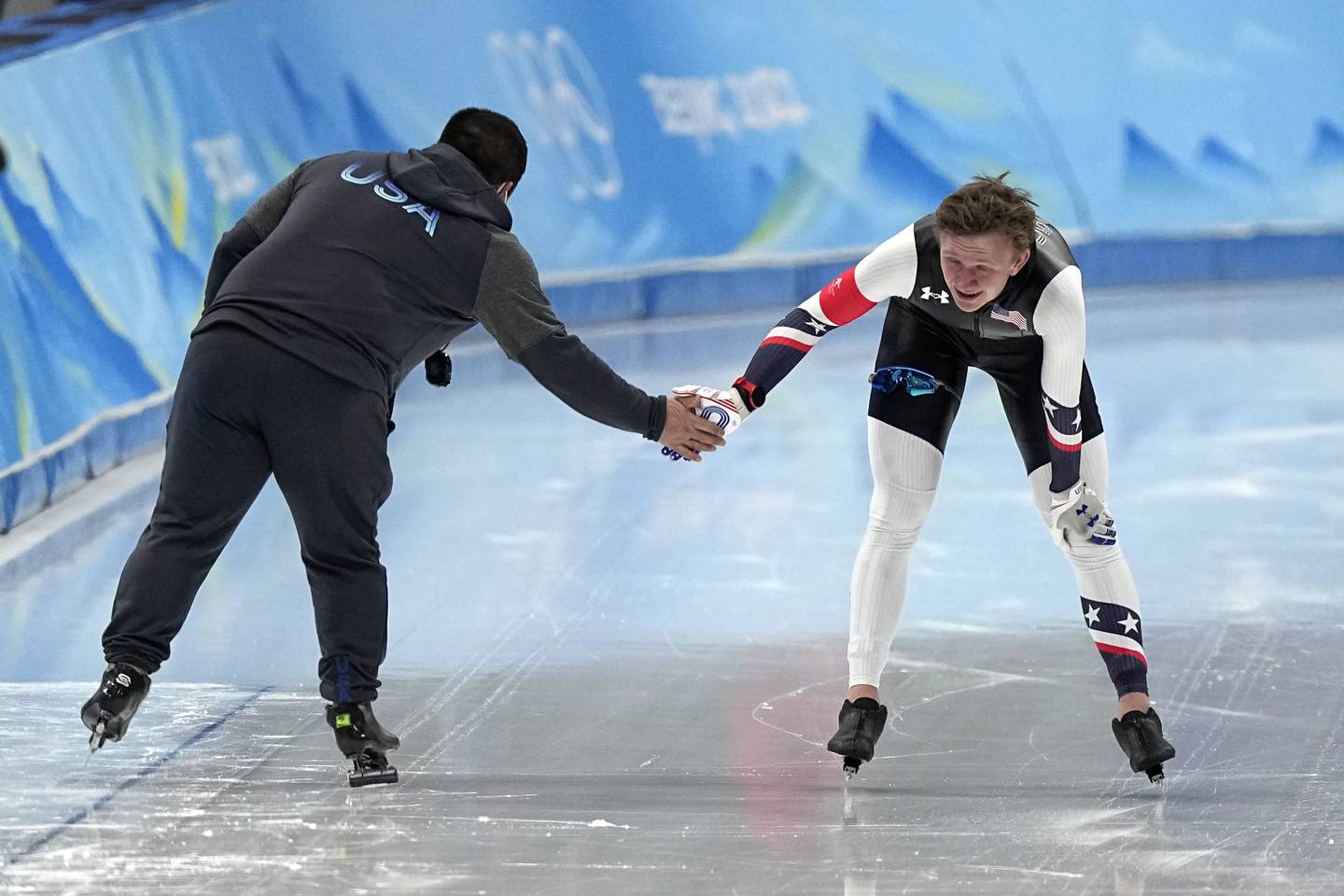 Ethan Cepuran of the United States is greeted by a coach after finishing his heat during the men's speedskating 5,000-meter race at the 2022 Winter Olympics, Sunday, Feb. 6, 2022, in Beijing. (AP Photo/Ashley Landis)