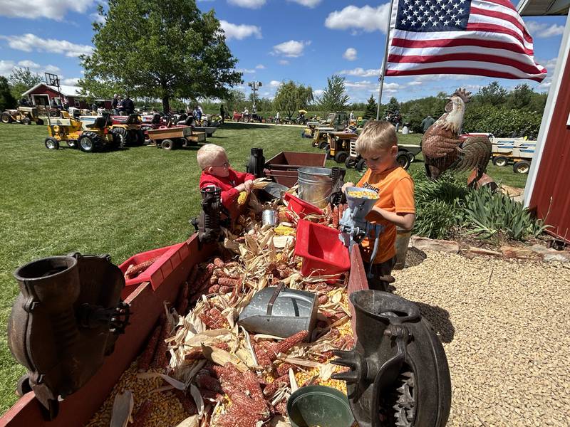 Easton James, 7, of Oregon, and Kyler Kitson, 8, of Harvard, run ears of corn through a hand sheller at the 16th Annual AJ’s Garden Tractor Jamboree on Saturday, May 17, 2025.