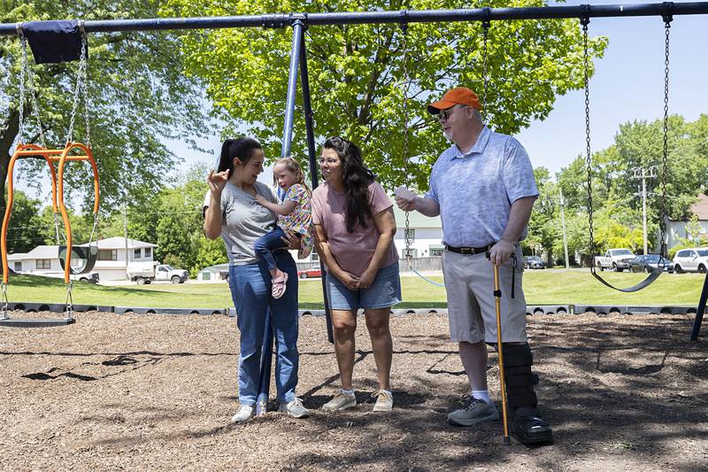 The guest of honor, Sophia Theobald, 4, is held by mom Nicole Theobald and supported by grandma and grandpa Shelly and Dan Long Friday, May 15, 2026, during the swing dedication.