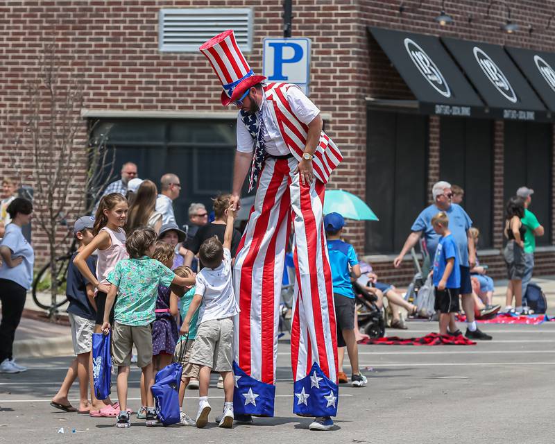 A stilt performer from the Lauren Underwood camp greets children at the annual PrairieFest parade in downtown Oswego. June 18, 2023.