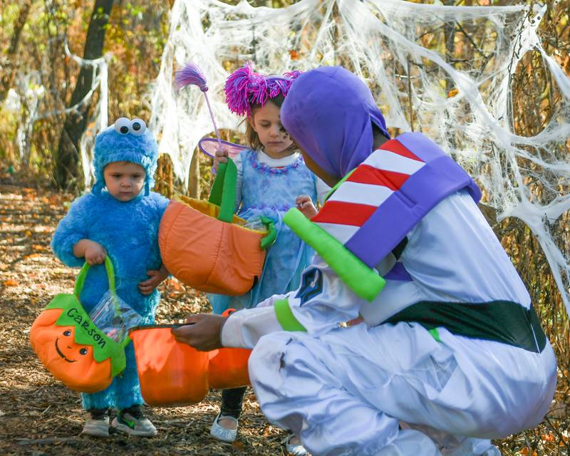 Carson Litterio, 2, left and sister Brooke Litterio, 4, of Glen Ellyn walk the Ackerman Park path in Glen Ellyn during The Boo Bash event on Saturday Oct. 26, 2024, and stopped off to get candy from Buzz Lightyear.