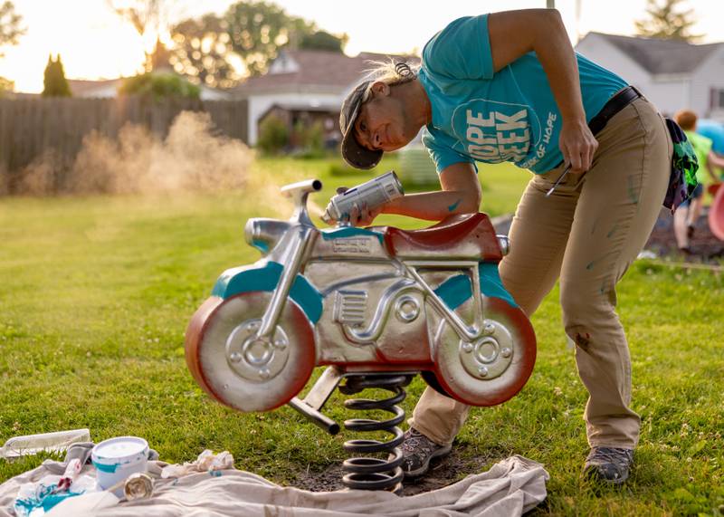 April Stevenson applies silver reflective paint for the chrome parts of the motorcycle while restoring playground equipment at Grand Ridge Park on June 4, 2025 in Grand Ridge.