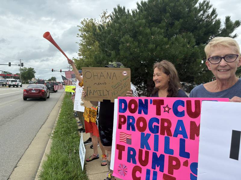 Protesters hold signs during a protest against President Trump along Route 31 in McHenry July 26, 2025.