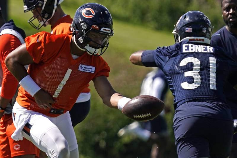 Chicago Bears quarterback Justin Fields, left, drops off the ball to running back Trestan Ebner during the NFL football team's training camp, Saturday, July 30, 2022, in Lake Forest, Ill.