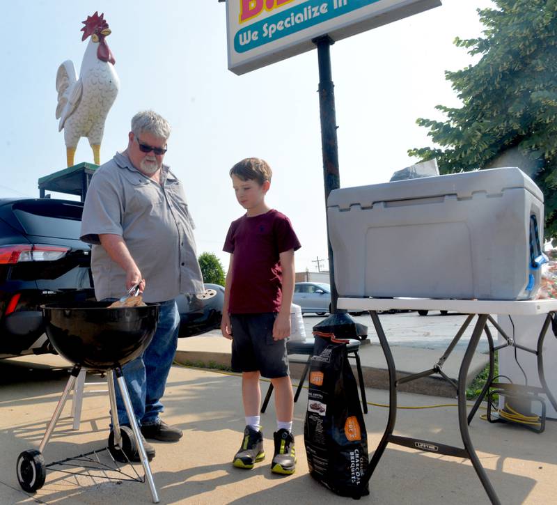 Braxton Cathey, 9, helps his dad Mike, grill chicken breasts on front of their restaurant B.B.Y. at the start of the Dixon City Market on Wednesday. In addition to food booths, the market includes a variety of other booths selling produce and other wares.