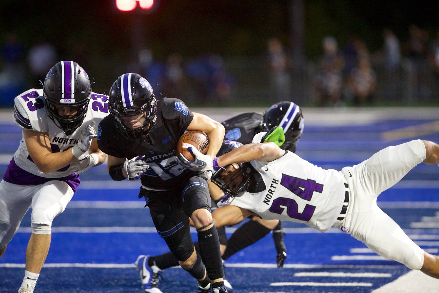 St. Francis's Darlo Millvojevic is tackled by Downers Grove North's Ethan Kist (23) and Ethan Murphy (24) on Friday, August 25, 2023 in Wheaton.