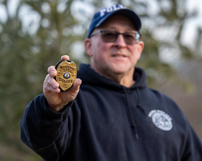 Retired Peru Police Sergeant Ed DeGroot poses for photo by extending arm to hold out badge on Monday, January 12, 2026. Sergeant DeGroot retired from the Peru police department after 30 years of service on January 2nd.