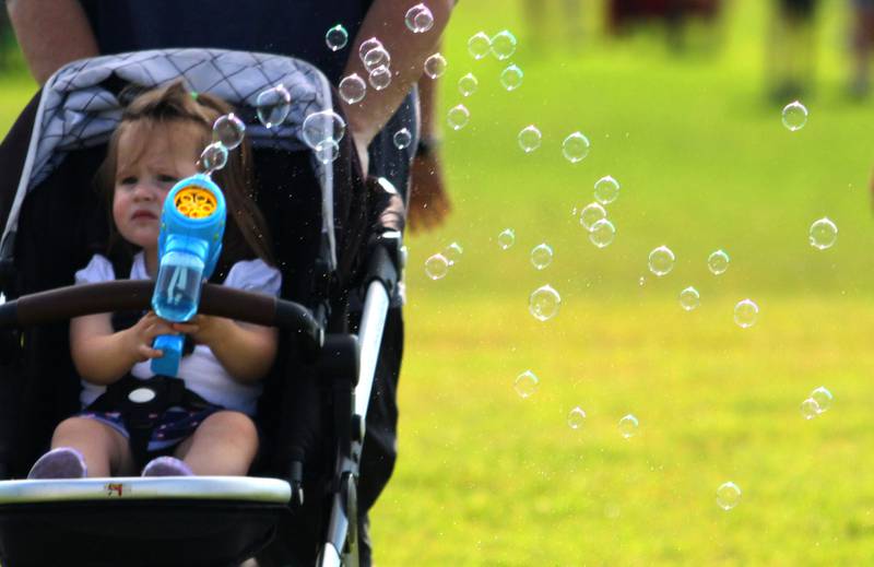 Maeve Jones, 2, of Cary leaves a wake of bubbles with her bubble machine as she cruises in her stroller during the Stars N’ Stripes Fest at Cary-Grove Park in Cary on Saturday, June 28, 2025.