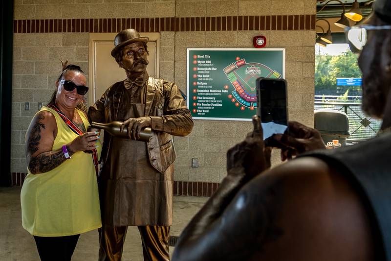Kevin Booker takes a photo of Jennifer Booker, from Will County Treasurer's Office, with a performance artist during New Orleans North Festival at Joliet Slammers Stadium on Aug. 15, 2025.