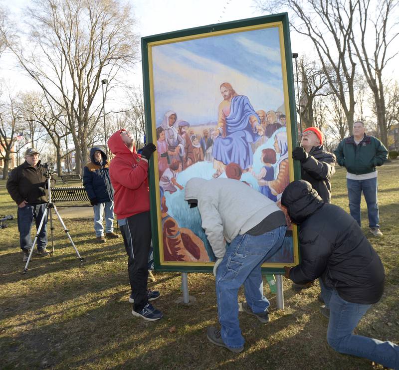 Volunteers lift to install 2 of the 16 paintings depicting the life of Christ Saturday in Ottawa’s Washington Square.The 4-foot by 7-foot paintings. The Ottawa Freedom Association has erected the paintings each year since 1992 after winning a lengthy court battle.