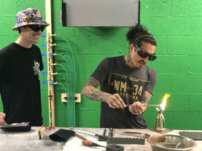 Kyle Myers, in training as a future glass blowing instructor, offers help to Marc Esses as the learns to shape molten glass at Otto’s in McHenry on July 18, 2022.