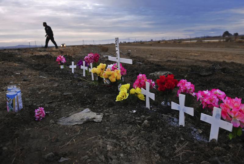 FILE - A row of crosses form a memorial along Highway 33 as police officers survey the scene a day after a crash killed nine people south of Coalinga, Calif., Saturday, Jan. 2, 2021. Investigators said the driver of an SUV involved in the crash was drunk and didn't have a license. The National Transportation Safety Board will use a final report on the crash to launch an effort to lobby for regulations requiring alcohol breath testing devices on all new vehicles. (Eric Paul Zamora/The Fresno Bee via AP)