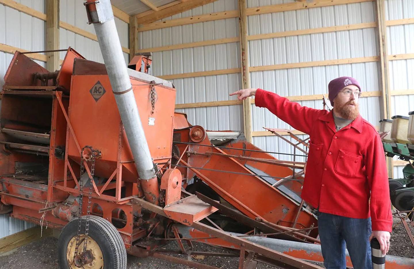 Grain farmer Jeff Hake gestures to an antique grain combine on his family’s McLean County farm, Funks Grove Heritage Fruits and Grains.