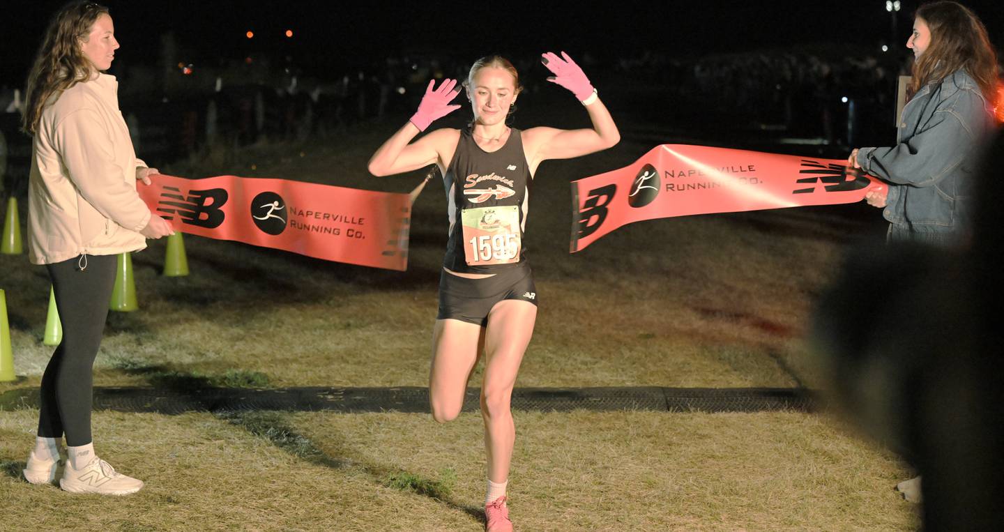 Sundara Weber, of Sandwich High School, breaks the tape to win the girls varsity race at the annual Naperville North Twilight Cross Country meet, this year at Settler’s Hill in Geneva on Wednesday, Oct. 8, 2025.