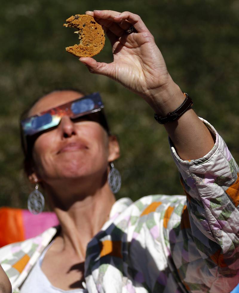 Colleen Bailey of Crystal Lake uses a cookie to show the shape of the eclipse as  she watchesthe partial eclipse Monday, April 8, 2024, at the Crystal Lake Park District's Nature Center.