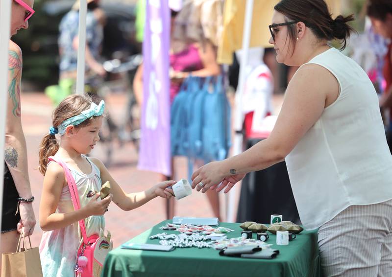 Natalie Cortese, 7, from Genoa, gets a sticker and a toy from Devyn Grzywa, a mortgage lender, at the FNBO booth during opening day for the DeKalb Farmers Market Thursday, June 1, 2023, at Van Buer Plaza in downtown DeKalb. The Farmers Market is open every Thursday from 10 am to 2 pm through September 21.