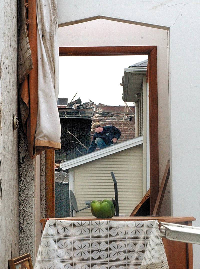 A view through a neighboring kitchen window, a Utica resident cleans the debris off of his roof following the April tornado.