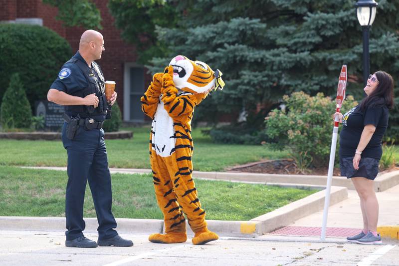The Herscher Tigers mascot, embodied by administrative assistant Kathy Astrella, interacts with Herscher Police Chief Kurt Quick, left, as the district welcomed Herscher Intermediate School students for the first day of school on Tuesday, Aug. 19, 2025. Crossing guard Michelle Ball, of Herscher, has a laugh as they wait for more students to arrive.