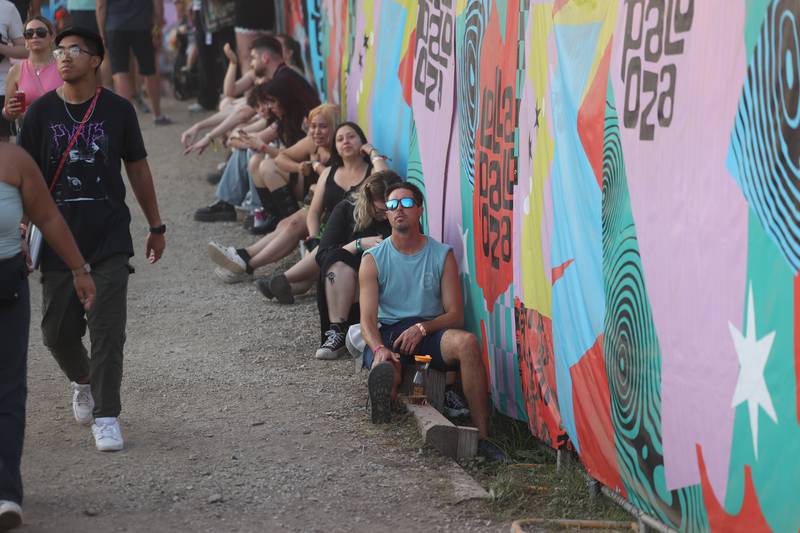 Festival goers use a curb to sit and listen to Pierce The Veil performs at Lollapalooza on Sunday, Aug. 4, 2024 in Chicago.