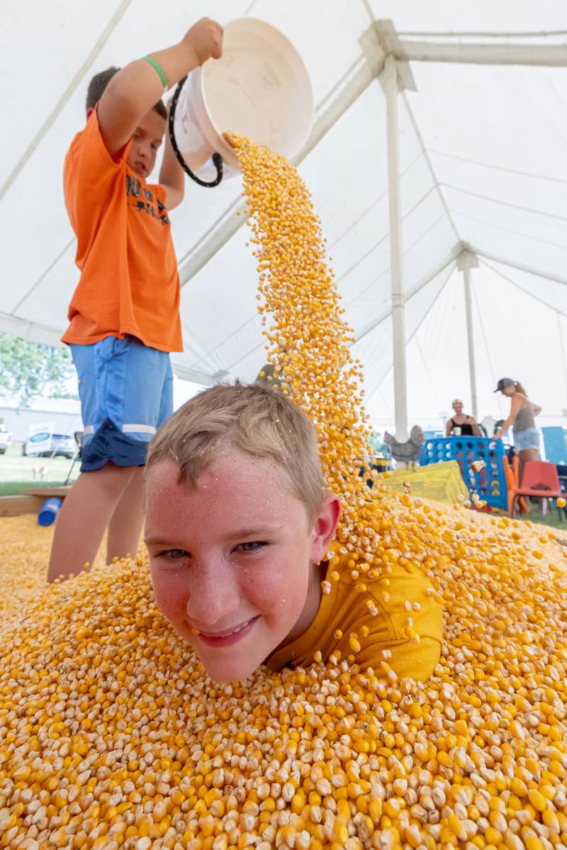 Parker Hettel (front) laughs as his friend Aaron Fulkerson attempts to bury him in the corn play area at the LaSalle County 4H Fair on July 10, 2025 in Ottawa.