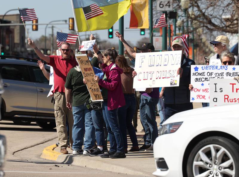 Protesters wave at passing cars on the corner of State and Main Street as they voice their displeasure with President Donald Trump Friday, March 14, 2025, in Sycamore. The group was protesting recent cuts by the Trump administration to the Department of Veterans Affairs.