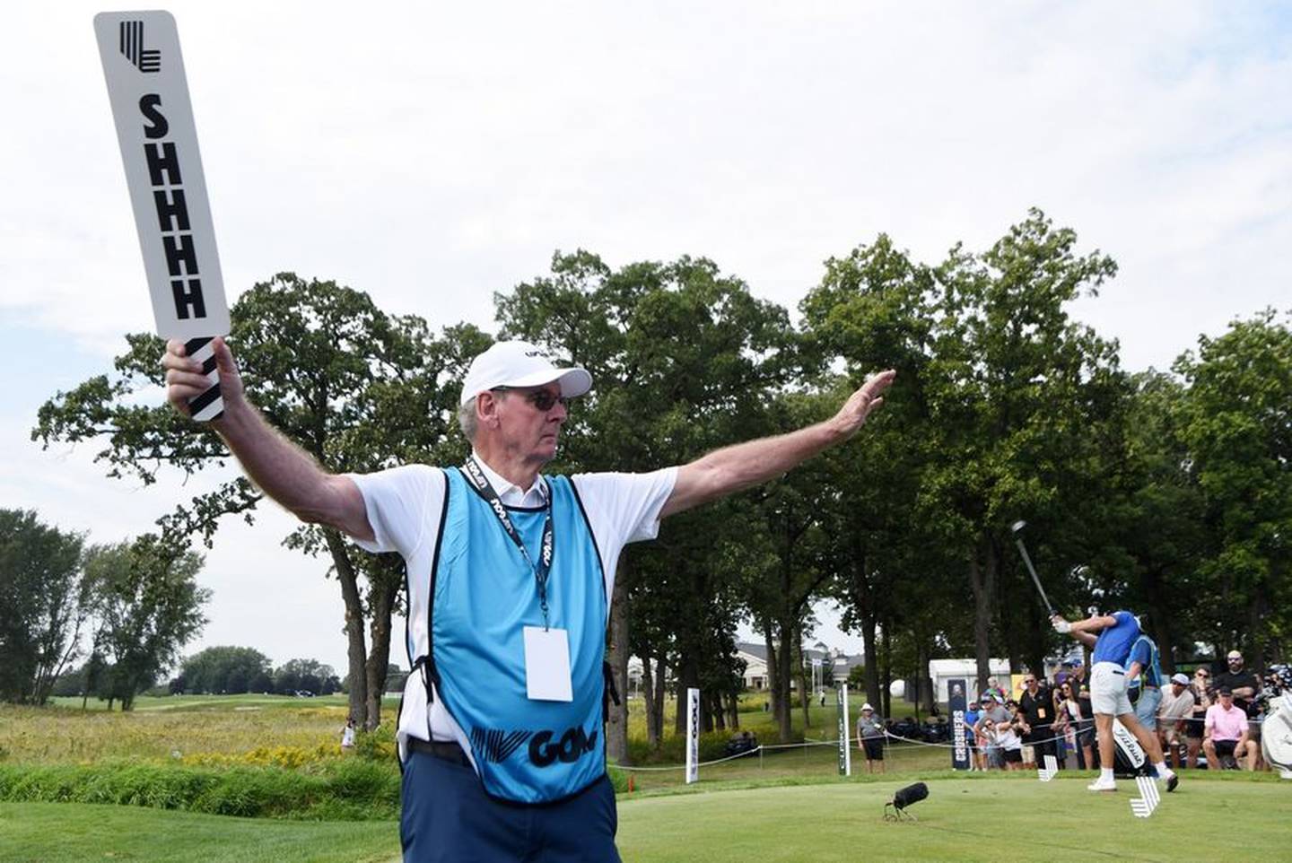 Golf marshal Bill Stewart of Palatine holds up a lighthearted version of a quiet sign while a golfer tees off during the LIV Golf Invitational Chicago 2022 in Sugar Grove Saturday. The sign says "Zip It" on the other side.