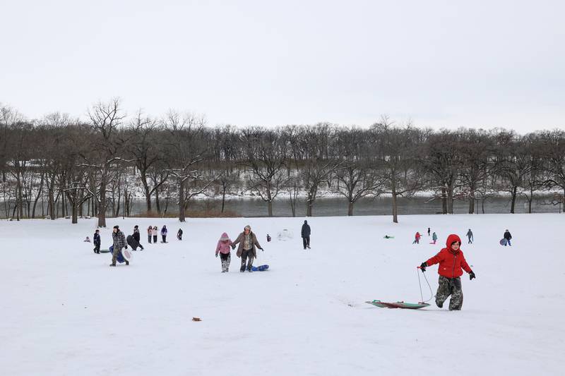 Sledders trek back up the hill at Helgeson Park in Bradley on Sunday, Nov. 30, 2025.