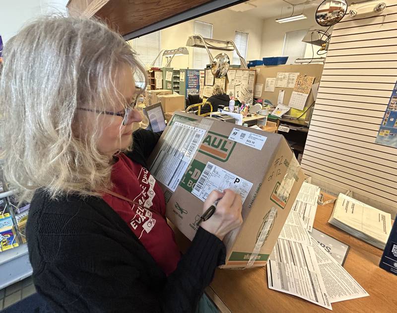 Joyce Long, chairman of the Outreach Team for the Evangelical Free Church of Mt. Morris, completes paperwork  on one of the 12 boxes filled with care packages for sailors on the USS Fitzgerald at the Mt. Morris Post Office on Thursday, Oct. 16, 2025. The postage to send the boxes was around $400.