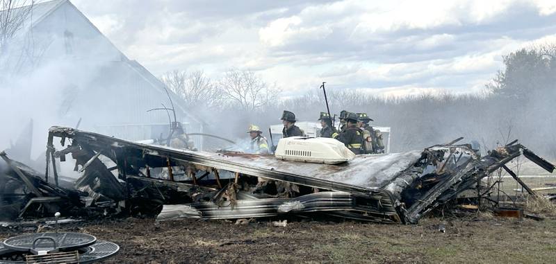Firefighters look for hot spots in a charred and collapsed recreational vehicle after a structure fire at 6727 W. Henry Road, southeast of Polo, on Wednesday, March 26, 2025. Several departments responded to the fire at the rural residence. In addition to the camper, one vehicle and other items located inside and around the garage were destroyed. No injuries were reported.