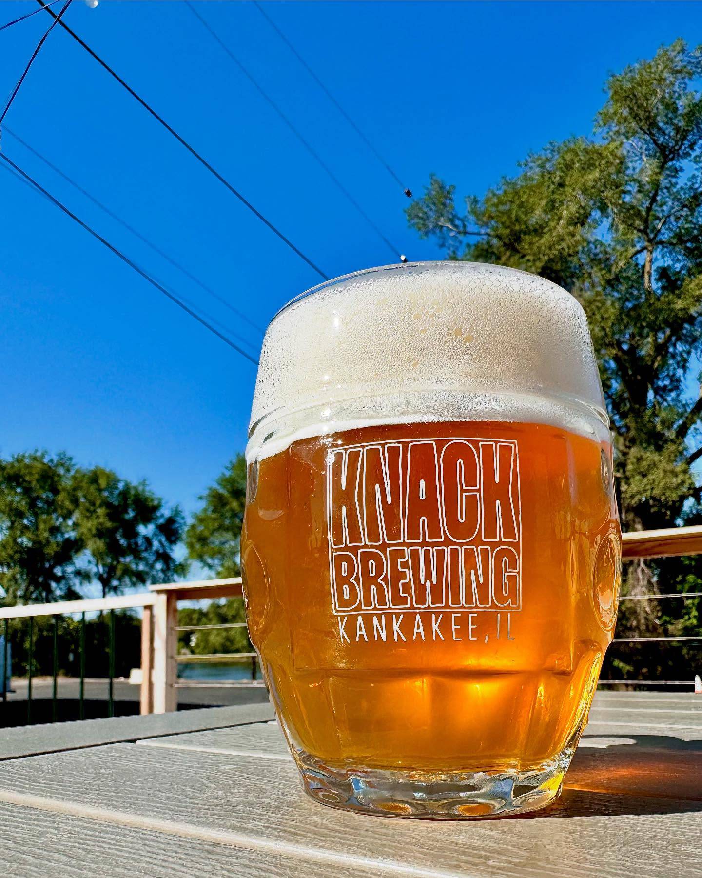 A Knack Brewing & Fermentations beer is pictured on the patio with the Kankakee River in the background.