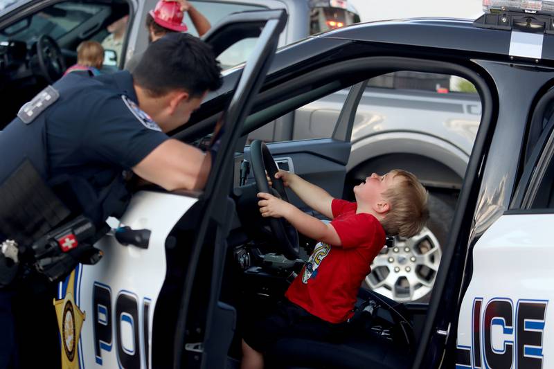 Zeke McEvoy, 2, of Crystal Lake enjoys his turn at the wheel of a police cruiser as Crystal Lake Police Officer Sal Alfano enjoys the moment during National Night Out activities in downtown Crystal Lake, Ill. on Thursday, August 7, 2025.