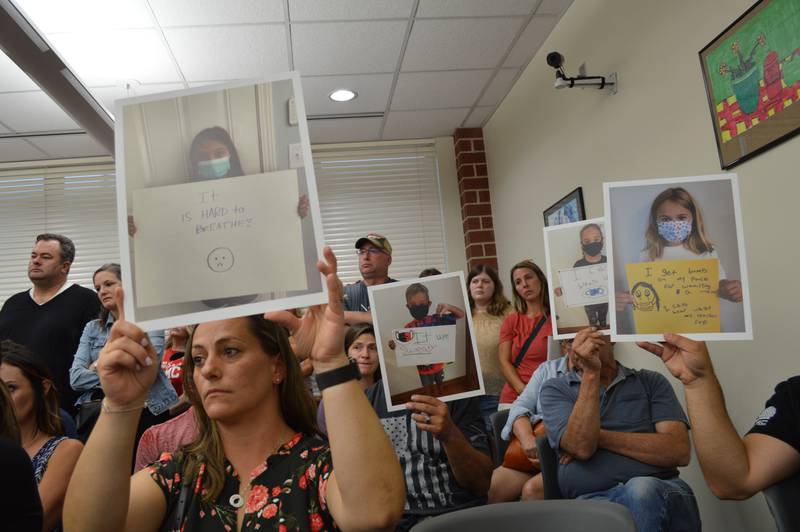 Aja Ferguson, front left, and others hold up photos of Huntley School District 158 students who were photographed with quotes about why they dislike wearing masks in schools at a school board meeting Thursday, July 15, 2021.