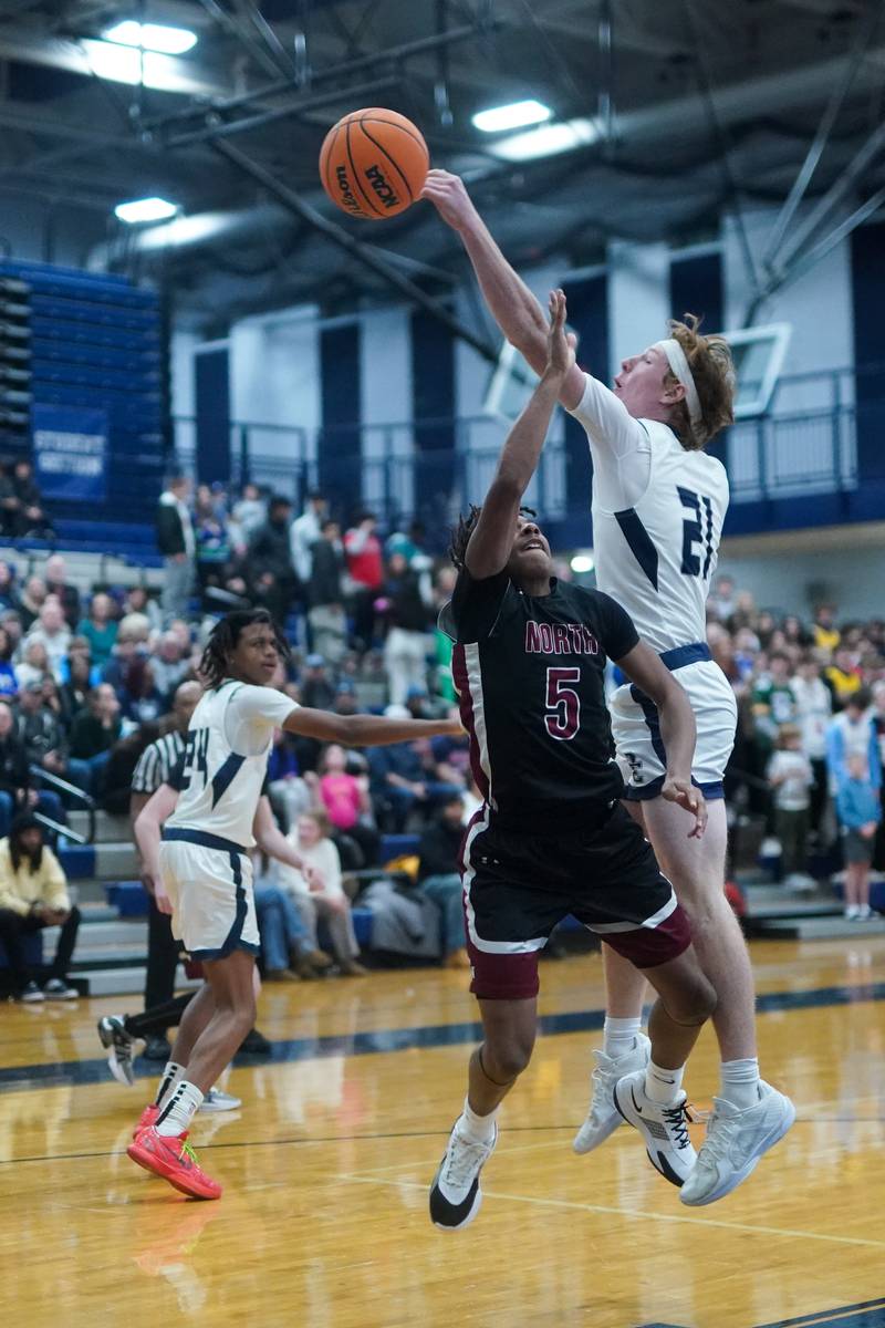 Oswego East's Andrew Pohlman (21) blocks a shot by Plainfield North's Darin Ashiru (5) during a basketball game at Oswego East High School on Friday, Dec. 6, 2024.