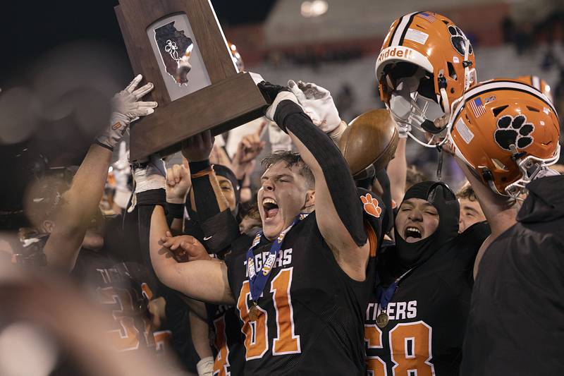 Byron’s Kade Politsch lifts the first place trophy as Byron celebrates their 56-50 win over Tolono-Unity Friday, Nov. 28, 2025, in the Class 3A football finals at Hancock Stadium at ISU.