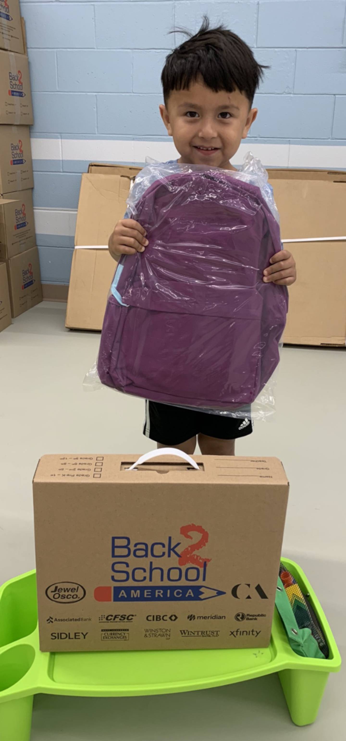 A P.H. Miller kindergarten student receives his free backpack from Costco and school supplies donated by the Kendall-Grundy Young Leaders.