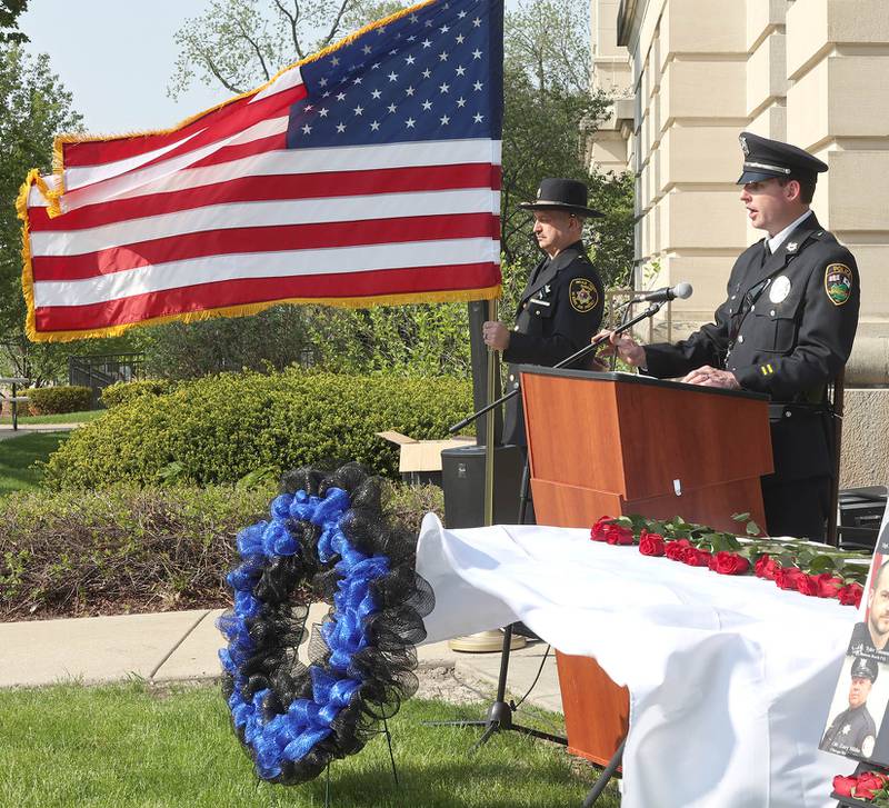 Sycamore Police Department Detective Ryan Hooper speaks as honor guard member DeKalb County Sheriff's Sergeant Tim Duda holds the flag Friday, May 13, 2022, during the DeKalb County Law Enforcement Officers' Memorial Service on the lawn of the DeKalb County Courthouse in Sycamore.