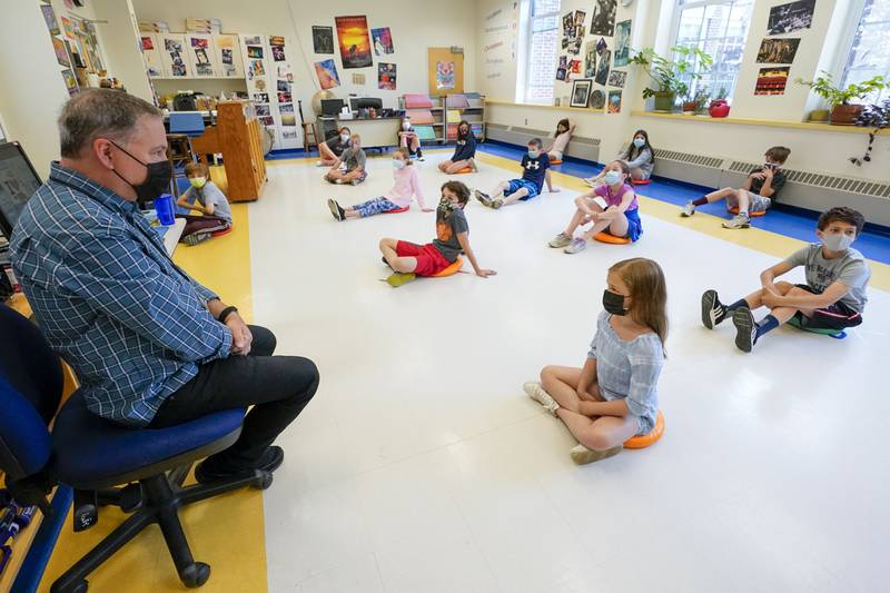 Fifth graders wear face masks and are seated at proper social distancing spacing in music teacher Marshall Toppo's, left, class at the Milton Elementary School, Tuesday, May 18, 2021, in Rye, N.Y. Milton reopened to full time, in-person learning in early March for the first time since the coronavirus outbreak. (AP Photo/Mary Altaffer)