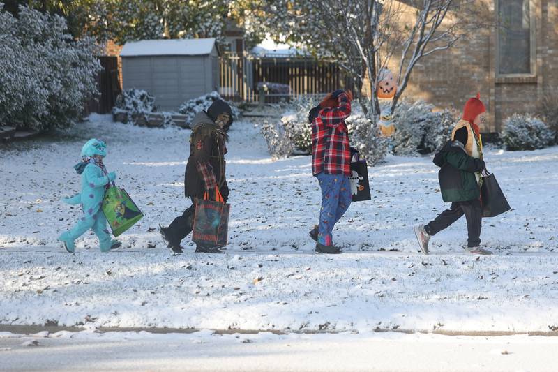 A trick-or-treaters walks along a snow covered sidewalk in a subdivision of Homer Glen on Tuesday, Oct. 31, 2023.