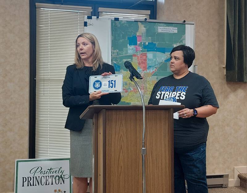 Princeton City Manager Theresa Wittenauer displays the license plates Monday, May 20, 2024, that are required for non-highway vehicles in the city. To her left is Gina Vujanov, treasurer of the Princeton High School Booster Club, which received a $3,000 donation from the city from the funds generated through the city's registration program.