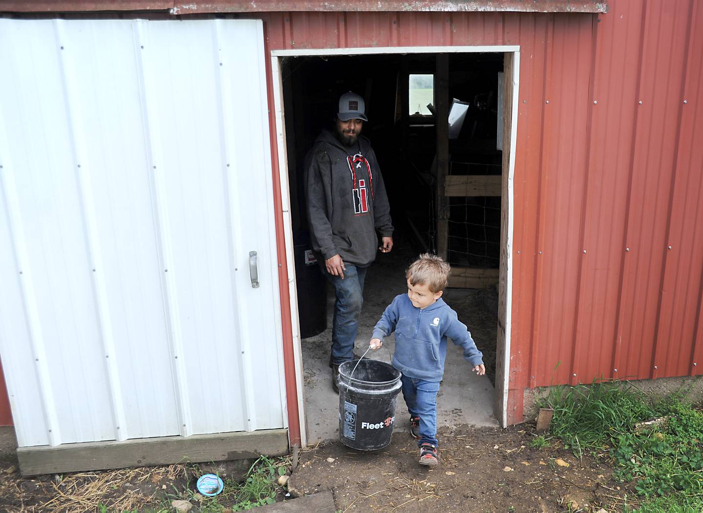 Farmer Bryon Kelly watches as his son, Rich, 2, carries a bucket of feed Friday, June 10, 2022, while feeding their cattle on the Jacobson farm near Richmond. Kelly inherited the century-old farm from his step-grandfather Richard Jacobson.