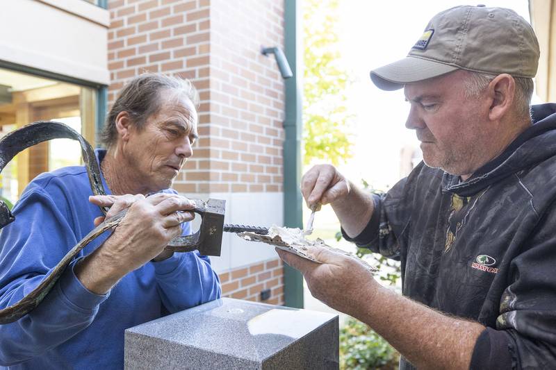 Local artist Mike McNamara (left) and Granite Works technician Dan Johns apply glue to sculpture work Monday, Oct. 20, 2025, in Franklin Grove. The sculpture dedicated to Winifred Knox is being put into place at the library.