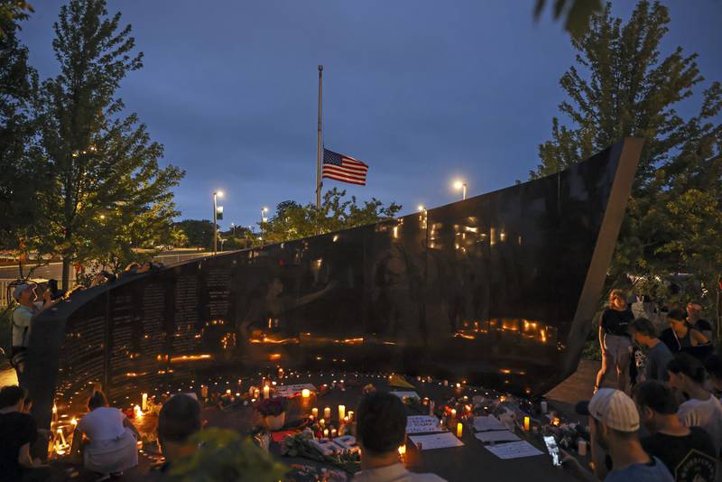 Dozens of mourners gather for a vigil near Central Avenue and St. Johns Avenue in downtown Highland Park, one day after a gunman killed at least seven people and wounded dozens more by firing an AR-15-style rifle from a rooftop onto a crowd attending Highland Park's Fourth of July parade, Tuesday, July 5, 2022 in Highland Park, Ill.. (Anthony Vazquez/Chicago Sun-Times via AP)