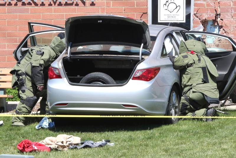 Officers in protective gear search a car Wednesday May 26, 2021, that crashed into the Sycamore Police Department on DeKalb Avenue. Law enforcement from several agencies are on hand investigating, and the cause of the crash remains unknown at this time.