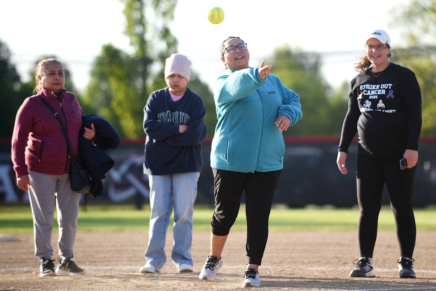 Angela Juarez, third from left, throws out a ceremonial first pitch of the Bradley-Bourbonnais and Bishop McNamara softball teams' Strikeout Cancer Night at their game in Bourbonnais Thursday, May 8, 2025. Watching Juarez, from left, are mother Araceli Oliva, daughter Alexis Ramos and Bishop McNamara softball coach Alee Rashenskas.