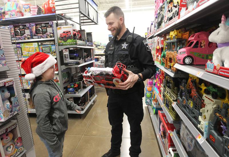 Annelyse Woodruff, 8, of Round Lake Park and Chris Schultz, auxiliary deputy with the Lake County Sheriff's Office, talk about toy firetrucks Dec. 12 during the Round Lake Park Shop with a Cop event at Walmart in Round Lake Beach.