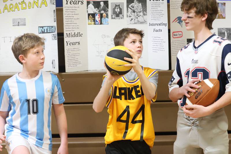 Logan Jr. High 6th grade students (from left) Liam Williams, as Diego Maradona, Jayce Ellberg as Jerry West, and Koby Berlinski as Tom Brady converse during a live Wax Museum on Thursday, Feb. 26, 2026 at Logan Jr. High School in Princeton.