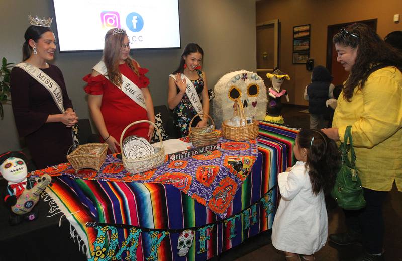Zoe Brown, 21, (Miss Lake County 2022) Cayden Zeller (Jr. Miss Round Lake Area 2022) and Darby Leetch, (Jr. Miss Round Lake Area 2021) both 14, greet Jaretzy Hernandez, 3, of Waukegan and her grandmother, Lilia Cervantes, as they were handing out masks and craft kits during the Day of the Dead Celebration at the Round Lake Beach Cultural & Civic Center.
