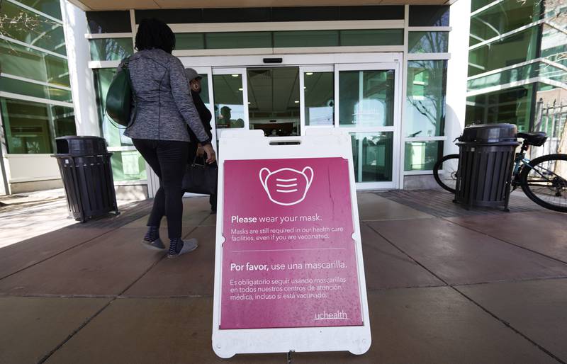 FILE - A sign advising visitors to don face coverings stands outside the main entrance to UCHealth University of Colorado hospital Friday, April 1, 2022, in Aurora, Colo.  COVID cases are starting to rise again in the United States, with numbers up in most states and up steeply in several. One expert says he expects more of a “bump” than the monstrous surge of the first omicron wave, but another says it’s unclear how high the curve will rise and it may be more like a hill.  (AP Photo/David Zalubowski, File)