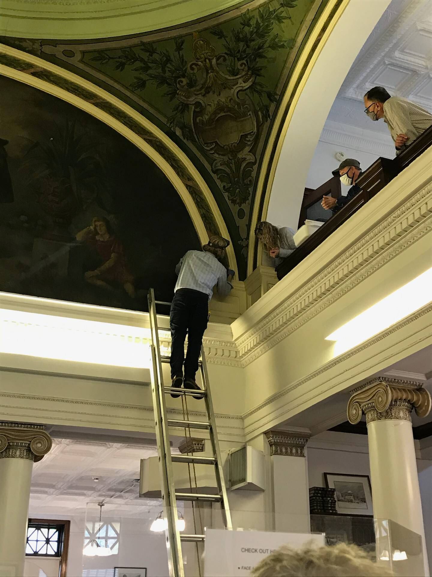 The library, which is listed on the National Register of Historic Places, will receive $139,075 in matching funds from the Institute of Museum and Library Services Save America’s Treasures grant program to restore its four murals. A representative from Parma Conservation of Chicago examines one of the murals as library trustees look on.