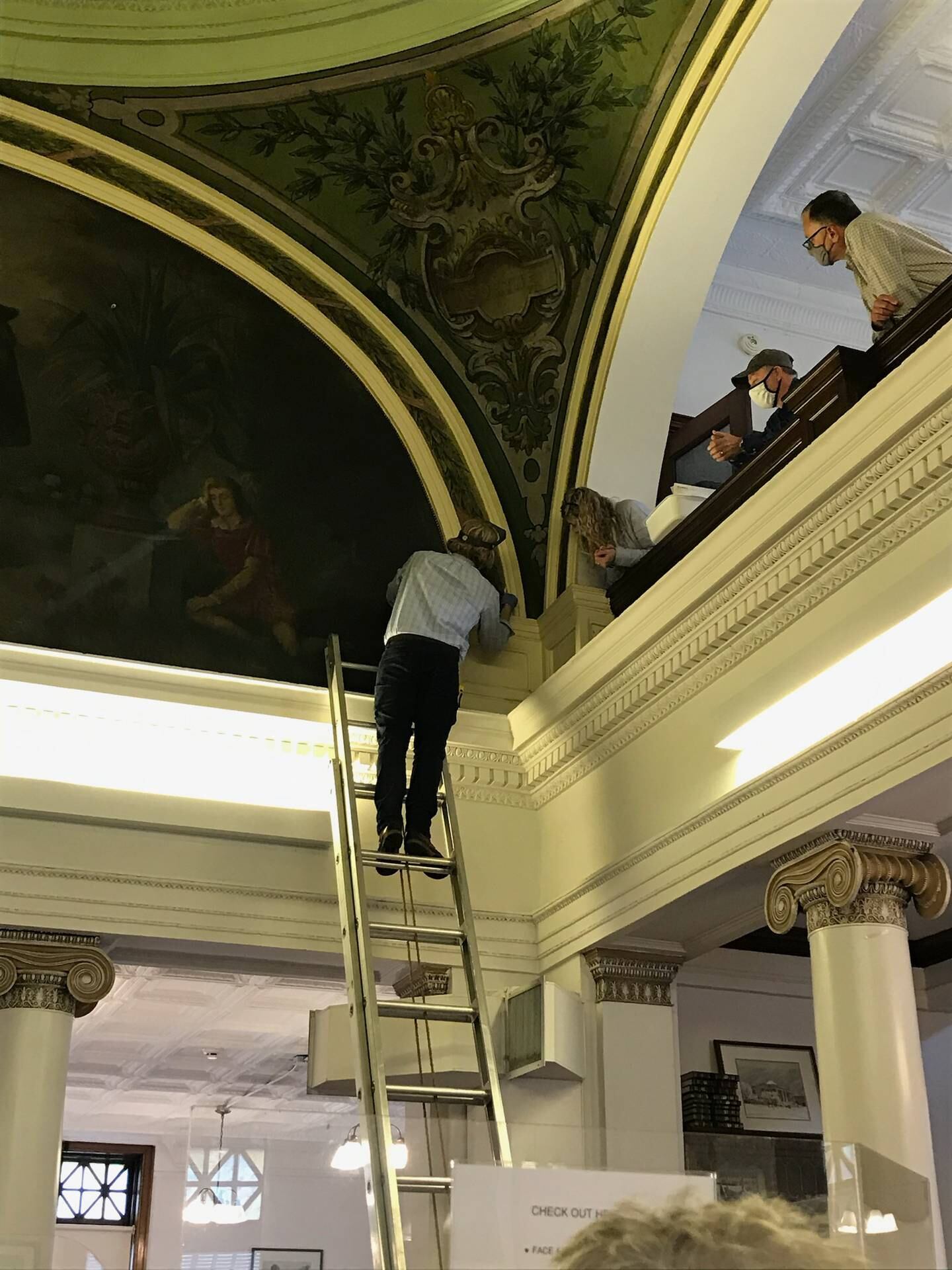 The library, which is listed on the National Register of Historic Places, will receive $139,075 in matching funds from the Institute of Museum and Library Services Save America’s Treasures grant program to restore its four murals. A representative from Parma Conservation of Chicago examines one of the murals as library trustees look on.